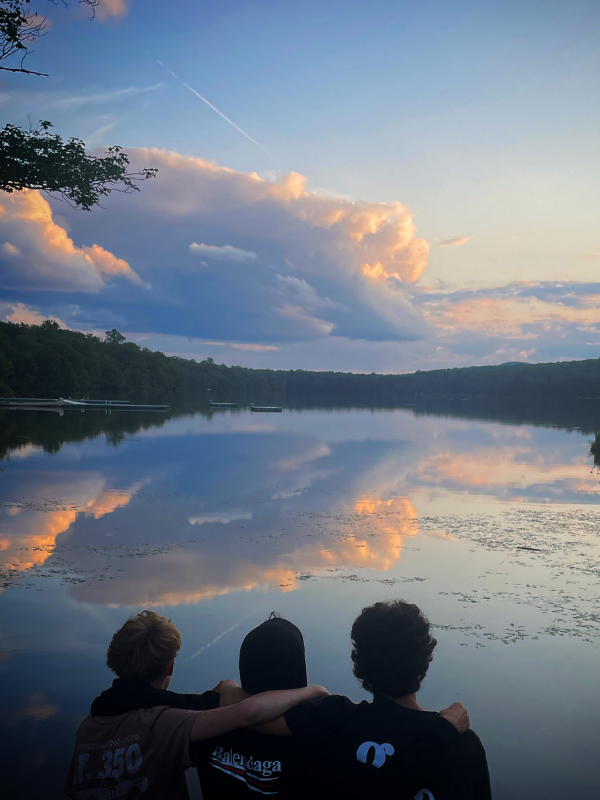Three boys sit with their arms around eachother watching the sun set over fairveiw lake