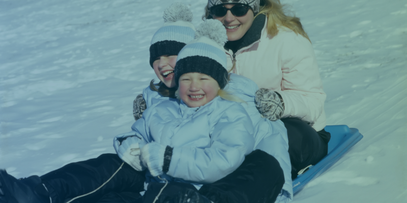Two girls and a woman sledding downhill in a winter landscape